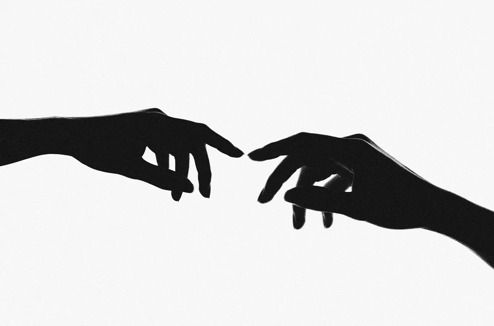 Two hands in silhouette reaching toward each other against a bright white background